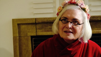 Marie-Luise O'Byrne-Brandl mit einem roten Gewand und einem Blumenkranz auf dem Kopf.