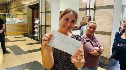 Sandra Hallen hält mit einem Lächeln einen Brief in die Kamera.