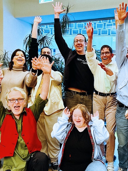 Eine Gruppe Menschen, zum Teil in Kostümen, winkt in die Kamera