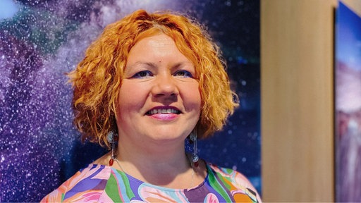 Liliya Gyrych steht vor einem Bild einer Galaxie und lächelt in die Kamera