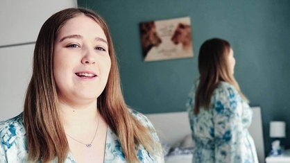 Chiara Orlowski, junge Frau mit dunkelblonden Haaren und grün-blau-weißem Oberteil, im Hintergrund sieht man sie im Spiegel von hinten.