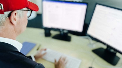 Frank W. sitzt an einem Schreibtisch vor einem Computer mit zwei Bildschirmen.