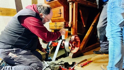 Ein Mann in Arbeitskleidung sitzt auf dem Boden und arbeitet an einem roten, runden Metallteil