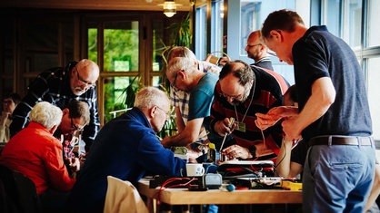 Mehrere Menschen stehen um einen Tisch herum, einige von ihnen werkeln mit Werkzeugen