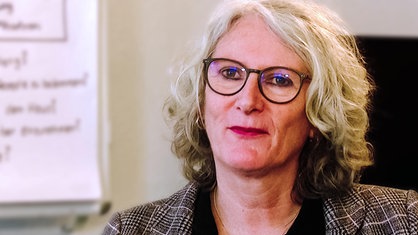 Eine Frau mit weiß-blondem Haar und Brille blickt nach vorne 