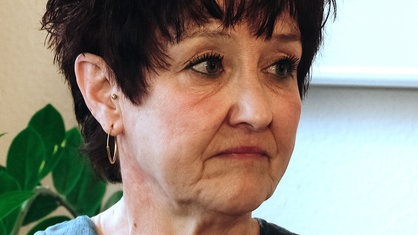 Eine Frau mit kurzen braunen Haaren blickt mit traurigem Gesicht nach rechts