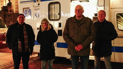 Drei Männer und eine Frau stehen vor einem Wohnmobil, es ist dunkel