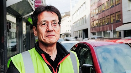 Eiichiro Kawasaki im Portrait neben parkenden Autos in der Innenstadt