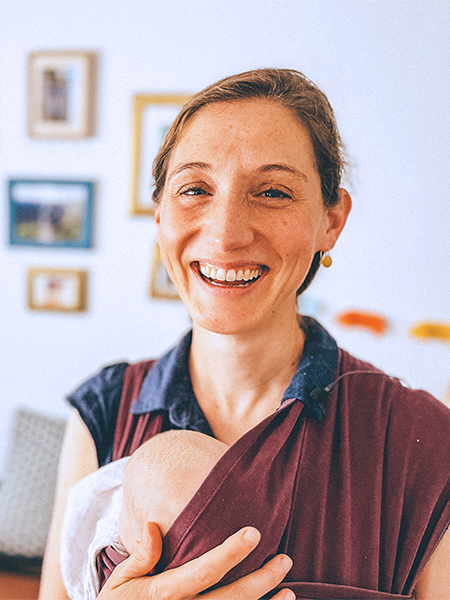 Links sitzt Mutter Greta auf der Couch, ein Baby im Arm. Rechts steht Anna van der Luijt, trägt ebenfalls ein Baby und lächelt.