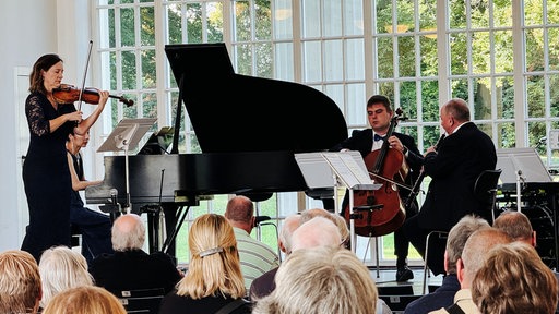 Das Staatsbad Orchester im Kurpark Bad Oeynhausen auf einer Bühne. Im Publikum sitzen einige Personen.