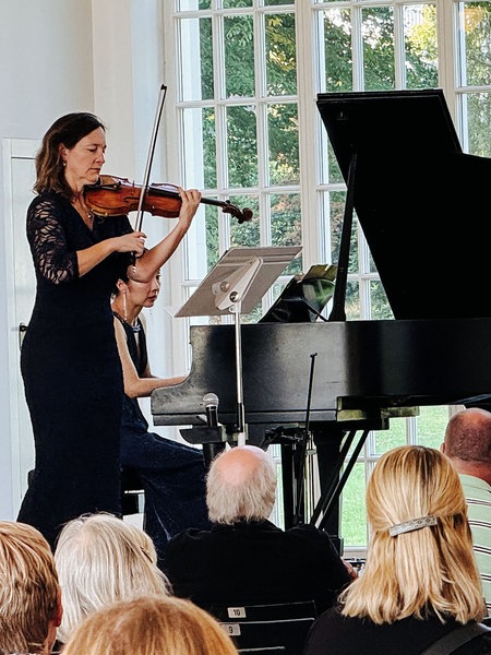Das Staatsbad Orchester im Kurpark Bad Oeynhausen auf einer Bühne. Im Publikum sitzen einige Personen.