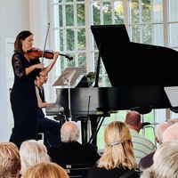 Das Staatsbad Orchester im Kurpark Bad Oeynhausen auf einer Bühne. Im Publikum sitzen einige Personen.