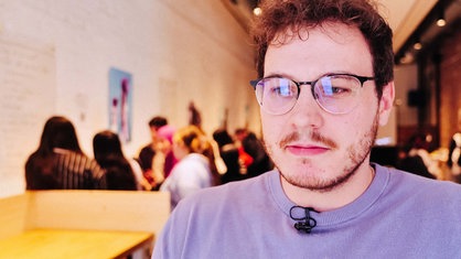 Collin Hauke steht in einem Raum mit geziegelten Wänden, im Hintergrund sitzen die Jugendlichen aus dem Nordsterne-Stipendium