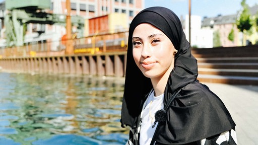 Nour Lahbitich trägt ein schwarzes Kopftuch und sitzt am Dortmunder Hafen.