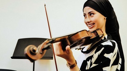 Auf dem Bild ist die 14-Jährige Nour Lahbitich zu sehen, die eine Geige spielt und dabei lacht.
