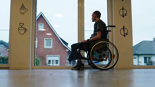 Ein Mann im Rollstuhl vor einem großen Fenster