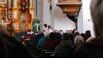 Ein Prieser in einer gut besuchten Kirche, man sieht die Kirchenbesucher in den Bänken nur von hinten