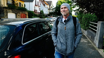 Henrik Strübli geht in seiner Nachbarschaft spazieren, er trägt Jacke, Mütze und auf dem Rücken einen Rucksack