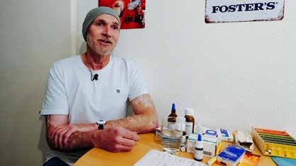 Henrik Strübli sitzt an seinem Küchentisch, darauf liegen viele Medikamente