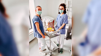 Xenia Look steht mit Lara Soyubey vor einem Tisch mit Spritzen und anderen Materialien zum Blutabnehmen