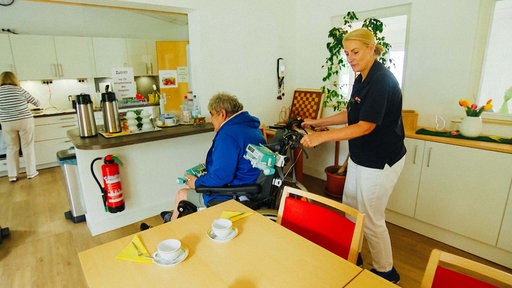 Krankenschwester Manuela Suler schiebt einen Hospiz-Patienten im Rollstuhl an einen Tisch.