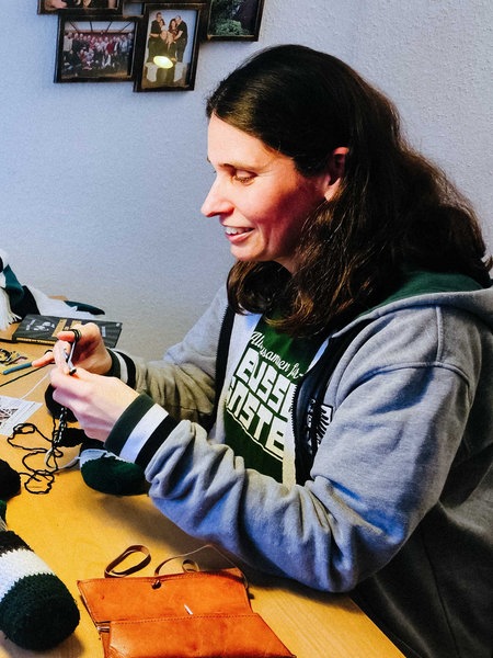 Zwei Frauen sitzen sich an einem Tisch gegenüber und häkeln. Zwischen ihnen liegt schwarz-weiß-grüne Häkelwolle.