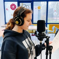 Cheyenne Erler steht beim Rap-Workshop im Klassenzimmer mit Kopfhörern vor einem Mikrofon. In der Hand hat sie einen Zettel mit ihrem Text.