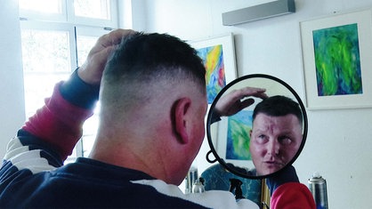 Ein Mann schaut in einen kleinen Spiegel und prüft seinen neuen Haarschnitt.