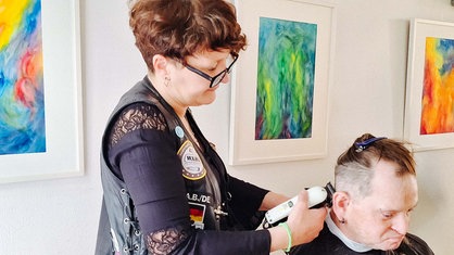 Eine Frau mit Brille schneidet einem Mann die Haare.