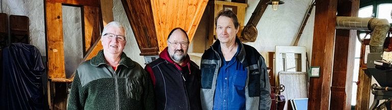 Günther Felten (Mitte) und zwei Ehrenamtler. Sie stehen im Dachstuhl einer Mühle.
