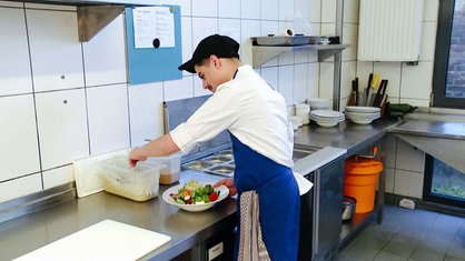 Salvatore Longobardo steht an einer Küchentheke. Er schöpft Salatsoße aus einem Plastikcontainer.