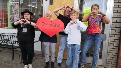 Vera Wipprecht und ihre Kolleginnen stehen vor dem Dorfladen in Hiddingsel. Vera Wipprecht hält ein großes rotes Papierherz in die Höhe.