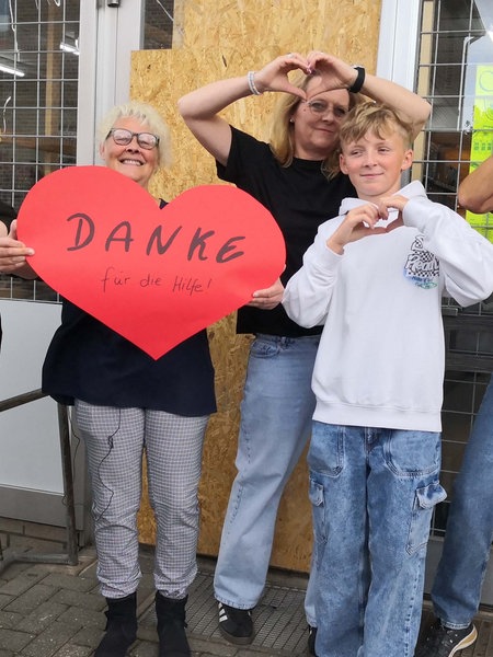 Vera Wipprecht und ihre Kolleginnen stehen vor dem Dorfladen in Hiddingsel. Vera Wipprecht hält ein großes rotes Papierherz in die Höhe.