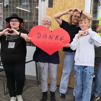 Vera Wipprecht und ihre Kolleginnen stehen vor dem Dorfladen in Hiddingsel. Vera Wipprecht hält ein großes rotes Papierherz in die Höhe.