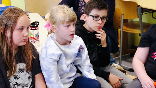 Schulkinder sitzen im Stuhlkreis nebeneinander.