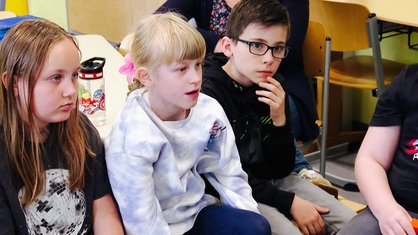Schulkinder sitzen im Stuhlkreis nebeneinander.