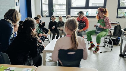 Ein Stuhlkreis mit Grundschülern und zwei Clowns