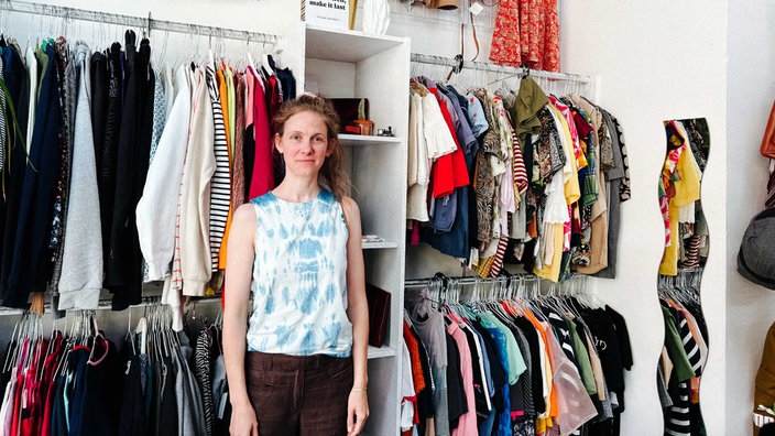 Ein Frau steht in einem Second-Hand-Laden für Kleidung.