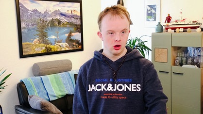 Marius Gottschalk, ein junger Erwachsener, mit Trisomie 21 steht in seiner Wohnung.