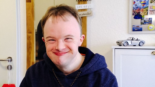 Marius Gottschalk, ein junger Erwachsener mit Trisomie 21 lächelt in die Kamera.