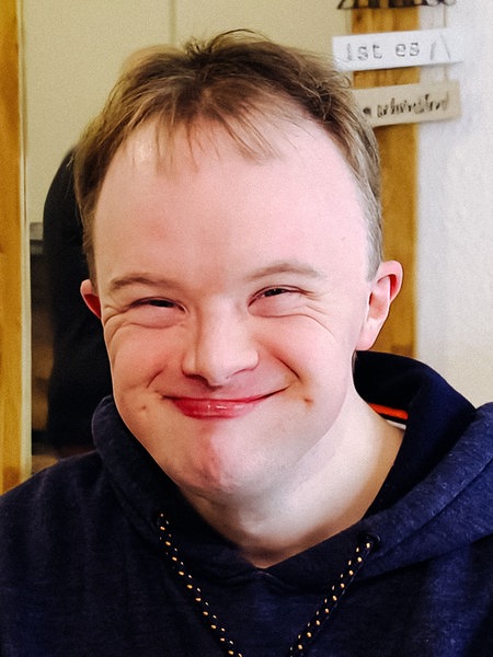 Marius Gottschalk, ein junger Erwachsener mit Trisomie 21 lächelt in die Kamera.