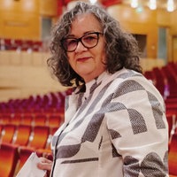 Silvia steht vor einer Sitzreihe der Essener Philarmonie. Das gesamte Gebäude ist menschenleer. In der rechten Hand hält sie ein ausgedrucktes Ticket. 