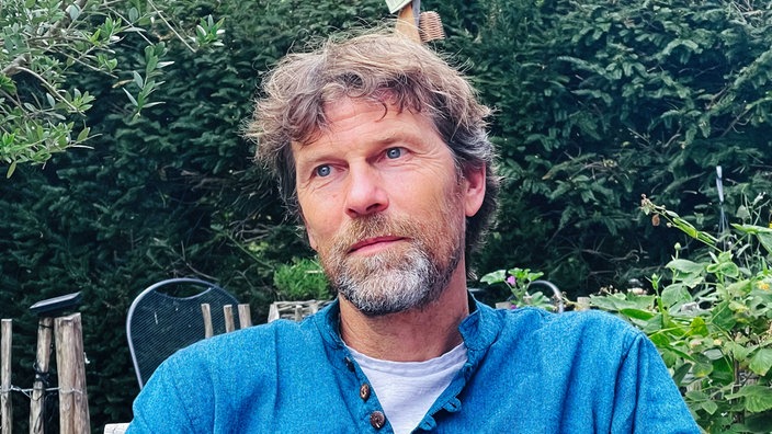 Ein Mann, Matthias Bäcker, in einem blauer Pullover sitzt in einem Garten.