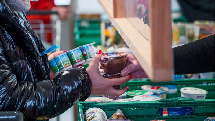 Eine Kundin bekommt an der Tafelausgabe Joghurt und Pudding.