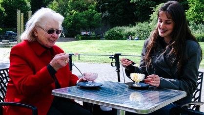 Die Schülerin Thea Zöller und die Seniorin Hanna Bause essen gemeinsam Eis und lachen.