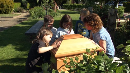 Pädagogin Karin Gerdemann und vier Kita-Kinder stehen auf der Trauerinsel auf dem Friedhof in Greven um das abgeschnittene Ende eines Sarges herum