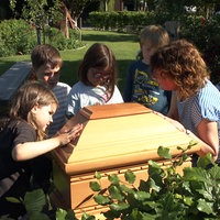 Pädagogin Karin Gerdemann und vier Kita-Kinder stehen auf der Trauerinsel auf dem Friedhof in Greven um das abgeschnittene Ende eines Sarges herum