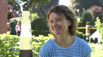 Heilpädagogin Karin Gerdemann sitzt auf der Trauerinsel auf dem Friedhof in Greven, im Hintergrund steht ein kleiner Leuchtturm
