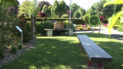 Ein Überblick über die Trauerinsel auf einem Friedhof in Greven mit einem Wackelbalken, einer Scheibe mit Labyrinth und dem Teil eines Sarges