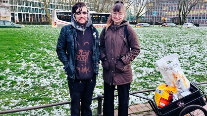 Ein Mann und eine Frau stehen nebeneinander, neben ihnen ein Handkarren mit Futter